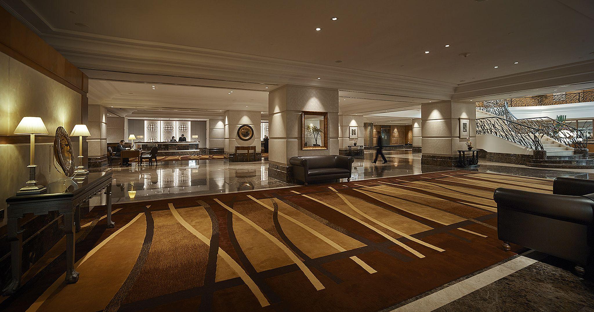 Sunway Putra Hotel Kuala Lumpur Exterior photo The photo depicts a spacious hotel lobby featuring modern and elegant decor. The floor has a stylish patterned rug in shades of brown and beige. There are several seating areas with dark leather couches. The lighting is soft and ambient, creating a w