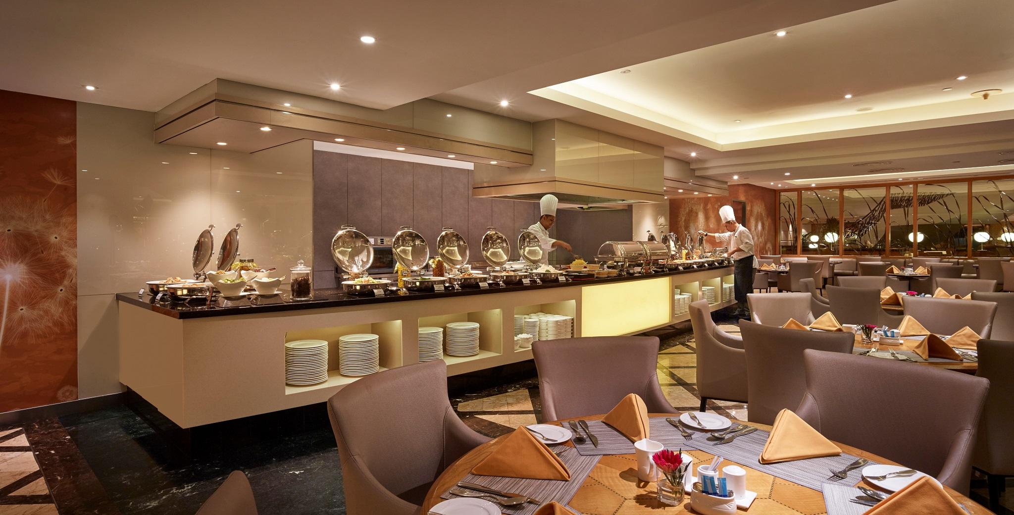 Sunway Putra Hotel Kuala Lumpur Exterior photo The photo depicts an elegant restaurant interior featuring a buffet setup. The buffet counter is lined with various food items in silver chafing dishes, indicating a selection of hot dishes available for guests. A chef in a white uniform is arranging