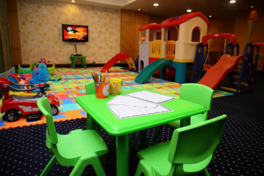 Sunway Putra Hotel Kuala Lumpur Exterior photo The photo shows a children's playroom. In the foreground, there is a small green table with four matching chairs, and on the table are some sheets of paper and coloring supplies like pencils. In the background, there is a colorful play structure with